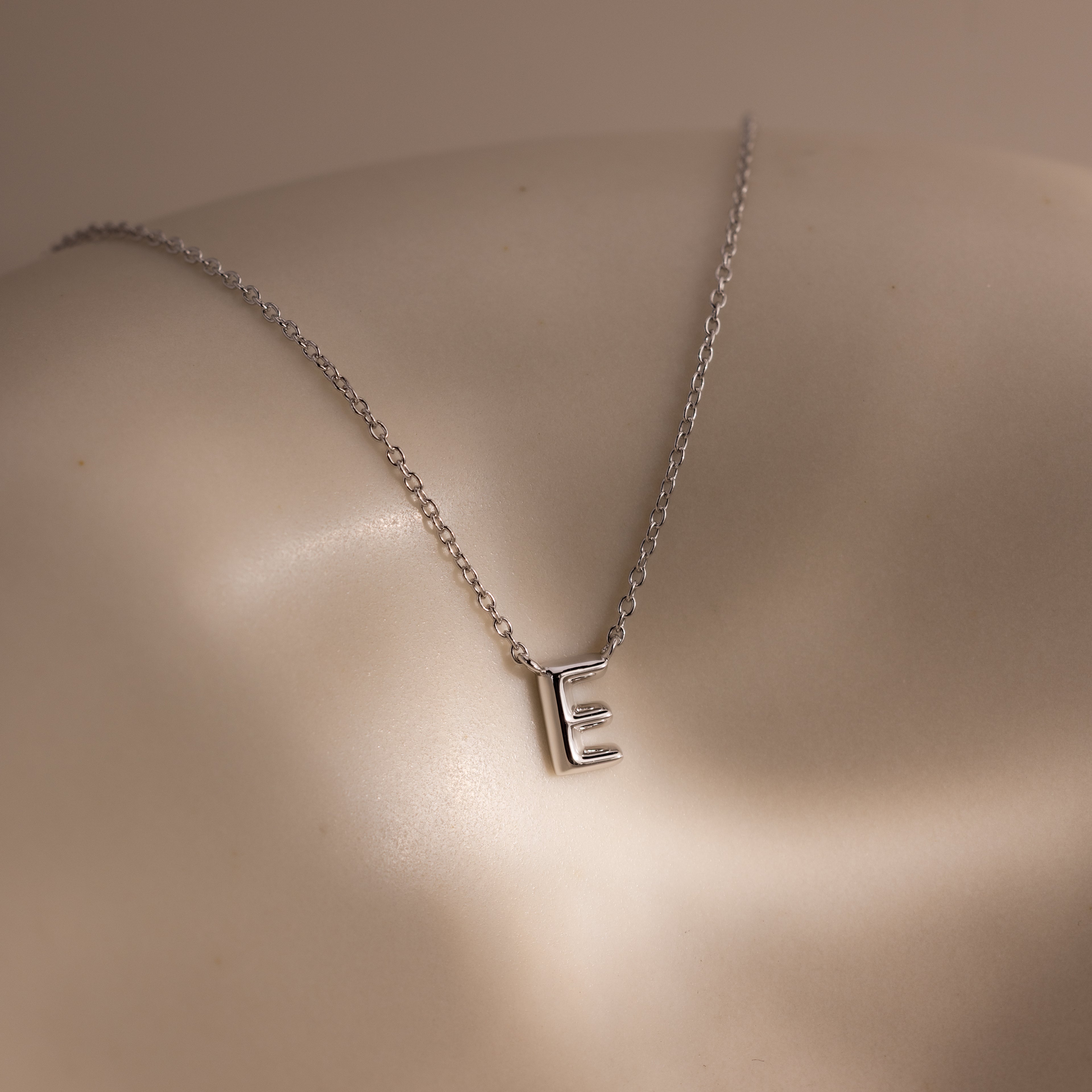 The Dainty Bubble Letter Necklace in Sterling Silver, shown with an "E" pendant on a smooth neutral background, is the perfect personalized minimalist accessory.