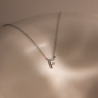 The Dainty Bubble Letter Necklace in Sterling Silver, featuring an F pendant, rests on smooth, softly lit skin—adding a touch of personalized elegance.