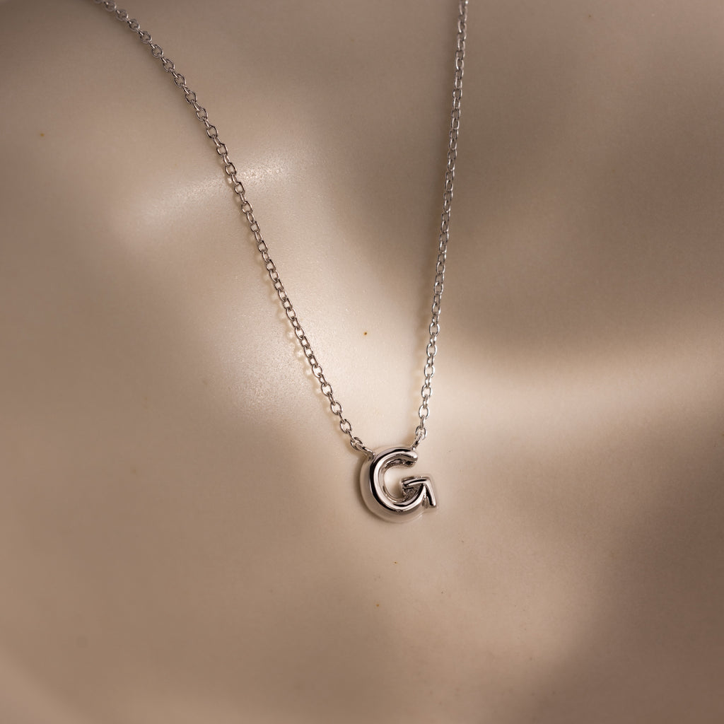 The Dainty Bubble Letter Necklace in Sterling Silver features a G-shaped pendant on a smooth, neutral background—an ideal choice for personalized, minimalist everyday style.