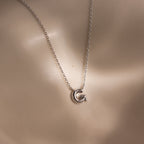 The Dainty Bubble Letter Necklace in Sterling Silver features a G-shaped pendant on a smooth, neutral background—an ideal choice for personalized, minimalist everyday style.