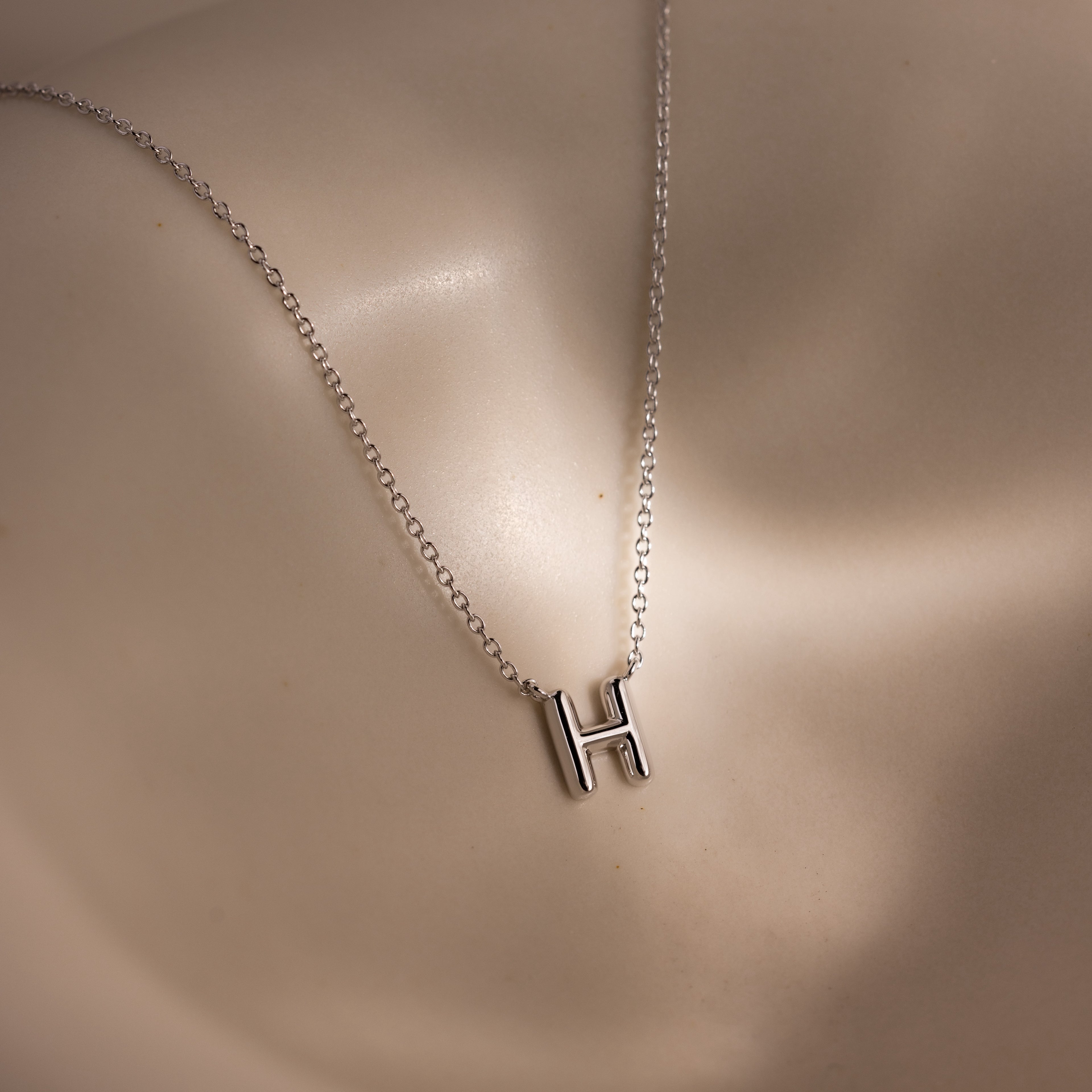 The Dainty Bubble Letter Necklace in Sterling Silver features a minimalist H pendant that rests beautifully on light skin, offering a personalized touch to any outfit.