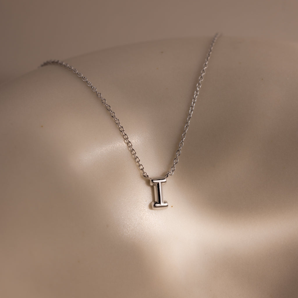 The Dainty Bubble Letter Necklace in Sterling Silver features a minimalist pendant shaped like the letter I, displayed on a smooth, neutral background.