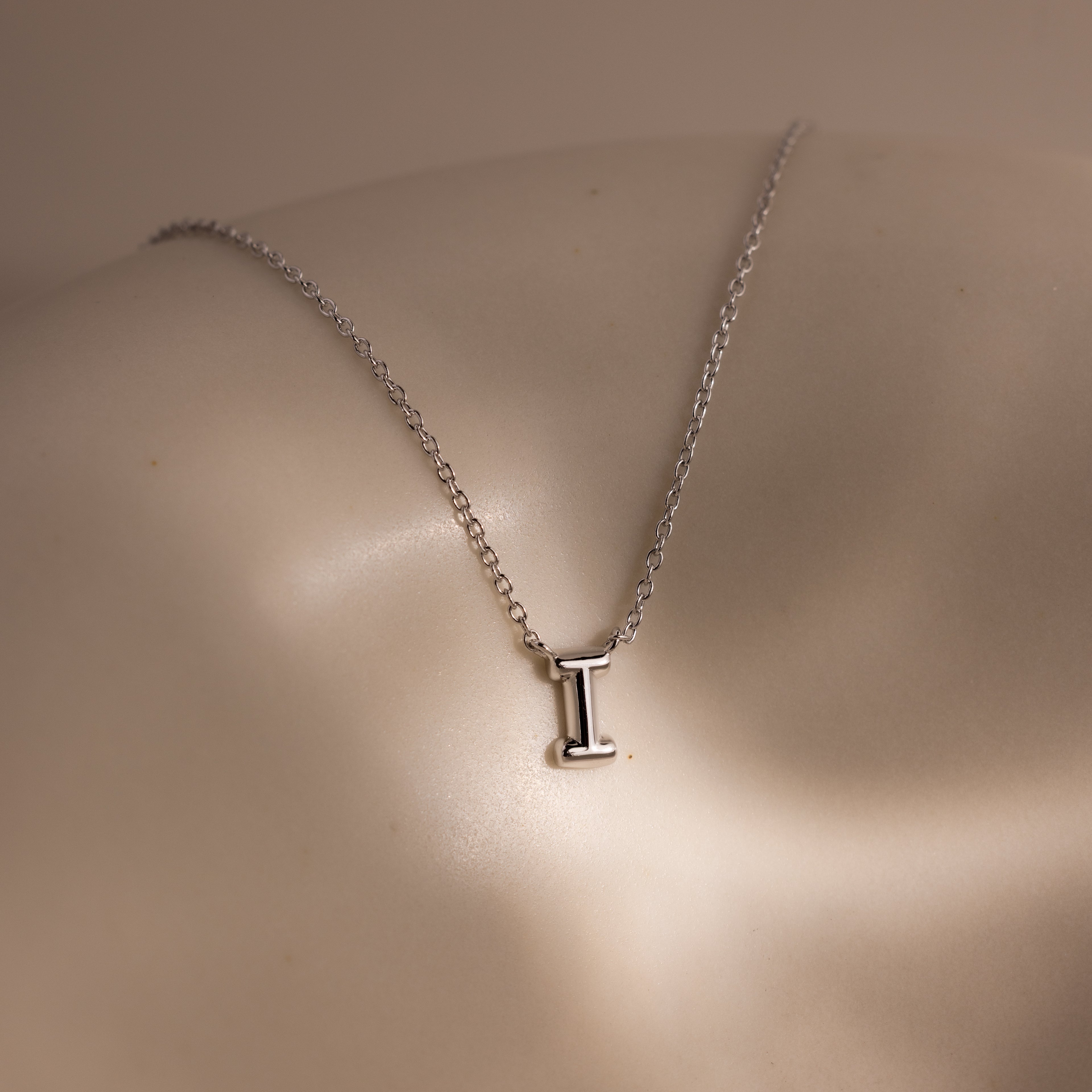 The Dainty Bubble Letter Necklace in Sterling Silver features a minimalist pendant shaped like the letter I, displayed on a smooth, neutral background.
