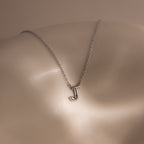 The Dainty Bubble Letter Necklace in Sterling Silver, featuring a J pendant, shines softly against light skin—an ideal personalized accessory for a minimalist style.