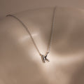 The Dainty Bubble Letter Necklace in Sterling Silver features a K-shaped pendant, resting on a smooth, light-colored surface to add personalized style to any minimalist look.