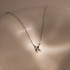 The Dainty Bubble Letter Necklace in Sterling Silver features a K-shaped pendant, resting on a smooth, light-colored surface to add personalized style to any minimalist look.