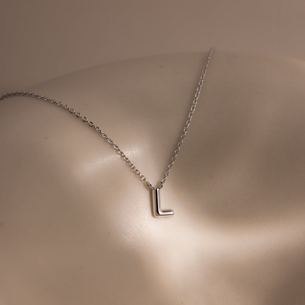 The Dainty Bubble Letter Necklace in Sterling Silver features an L pendant, shown resting on smooth, light-toned skin under soft lighting—a perfect minimalist piece to express your personal style.
