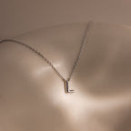The Dainty Bubble Letter Necklace in Sterling Silver features an L pendant, shown resting on smooth, light-toned skin under soft lighting—a perfect minimalist piece to express your personal style.