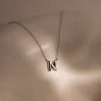 The Dainty Bubble Letter Necklace in Sterling Silver, featuring a bubble letter N pendant, is showcased on smooth, light-colored skin under soft lighting.
