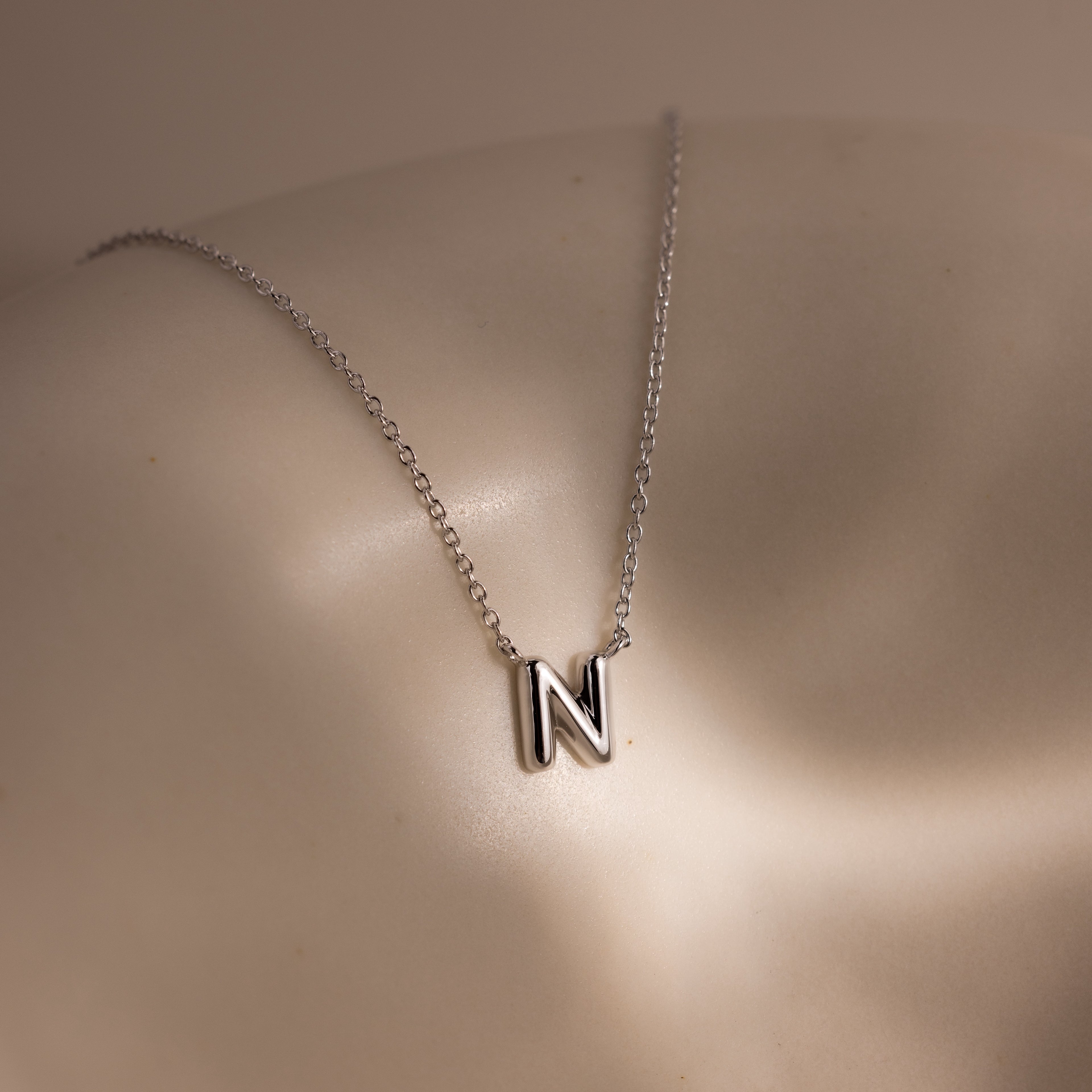 The Dainty Bubble Letter Necklace in Sterling Silver, featuring a bubble letter N pendant, is showcased on smooth, light-colored skin under soft lighting.