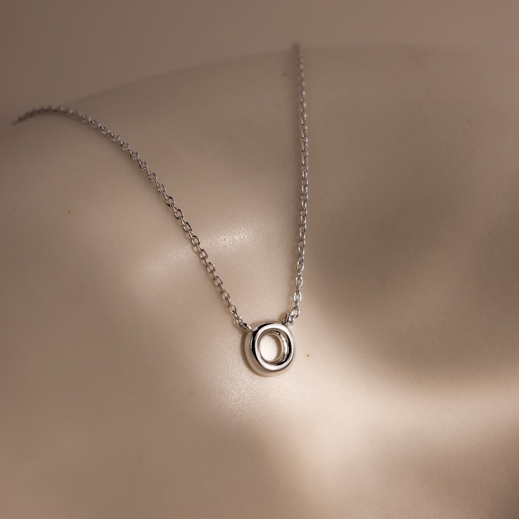 Dainty Bubble Letter Necklace in Sterling Silver featuring a bubble letter pendant, displayed on a smooth, curved surface under soft lighting.