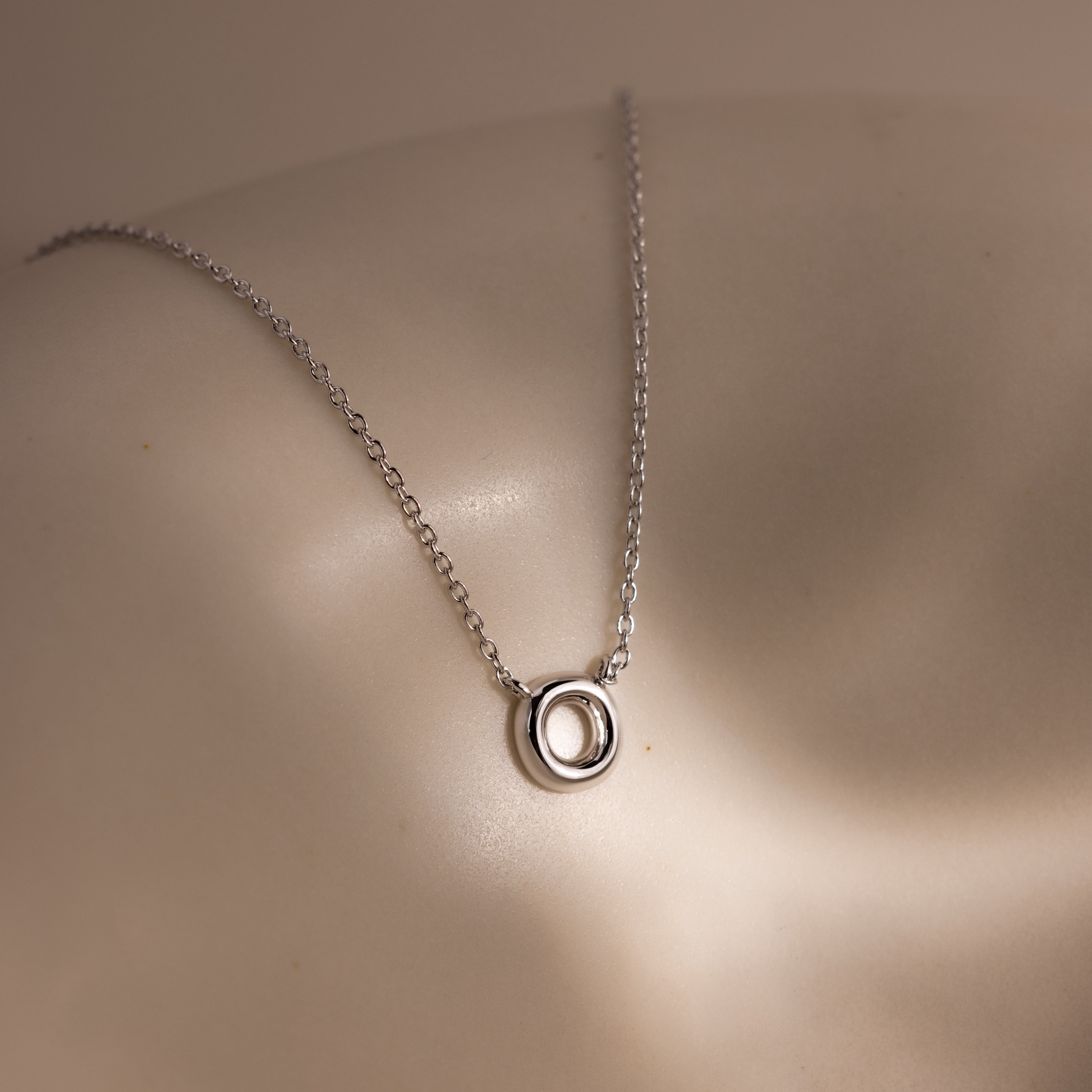 Dainty Bubble Letter Necklace in Sterling Silver featuring a bubble letter pendant, displayed on a smooth, curved surface under soft lighting.