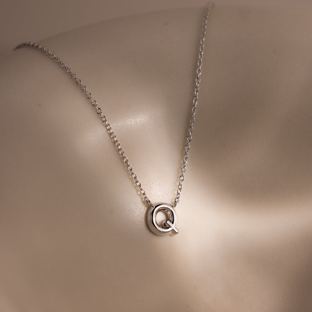 The Dainty Bubble Letter Necklace in Sterling Silver features a silver letter Q pendant in a minimalist bubble style, displayed on a light surface—an elegant, personalized accessory for everyday wear.