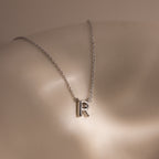 Dainty Bubble Letter Necklace in Sterling Silver featuring an R pendant, showcased on smooth, beige skin under soft lighting.