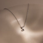 The Dainty Bubble Letter Necklace in Sterling Silver features a minimalist silver S pendant, resting elegantly on pale skin under soft lighting.