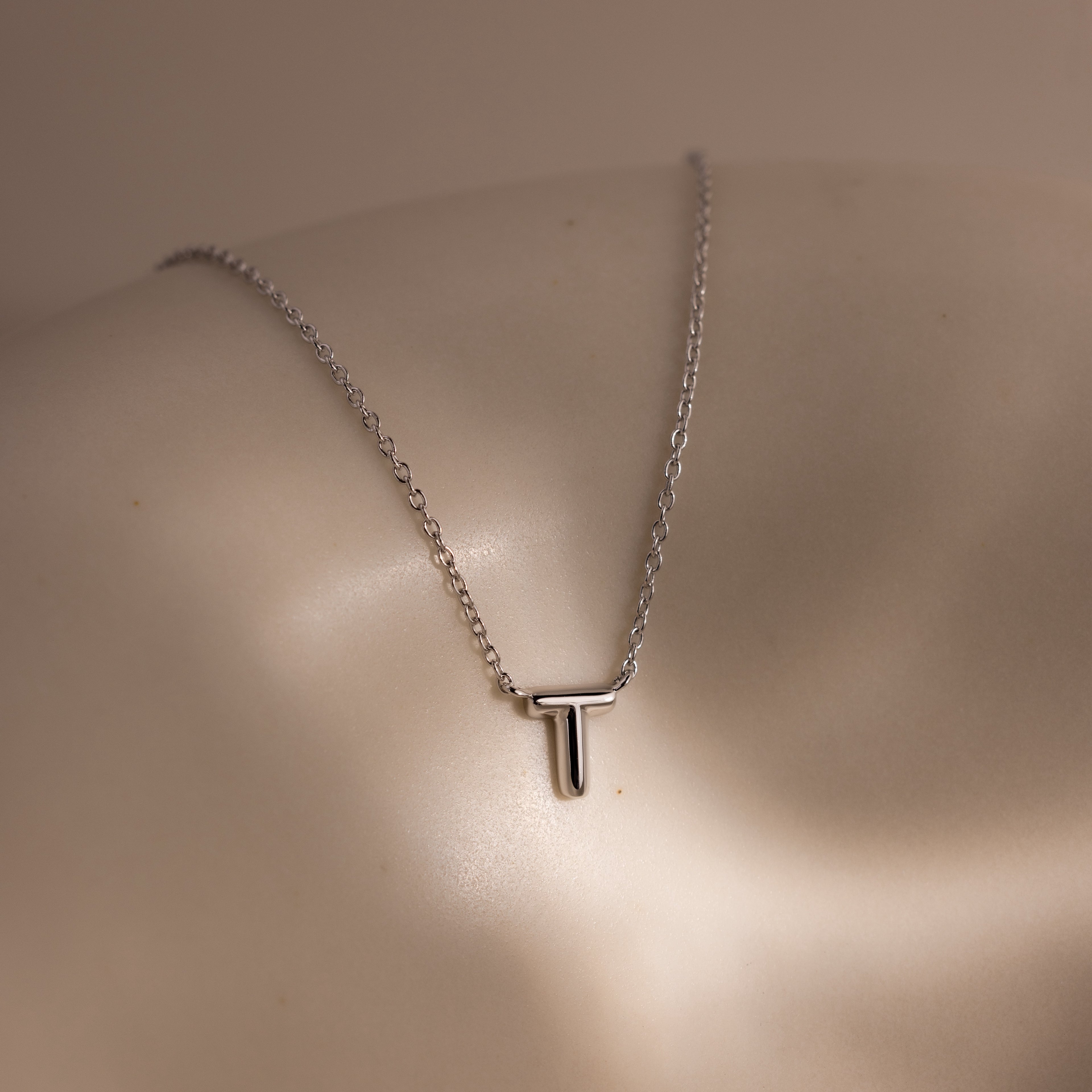 Dainty Bubble Letter Necklace in Sterling Silver, featuring a personalized initial pendant on a sleek silver chain, elegantly displayed on a smooth, neutral surface—ideal for lovers of minimalist and custom jewelry.