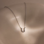 Dainty Bubble Letter Necklace in Sterling Silver with a minimalist design, shown on a smooth, light-colored surface.