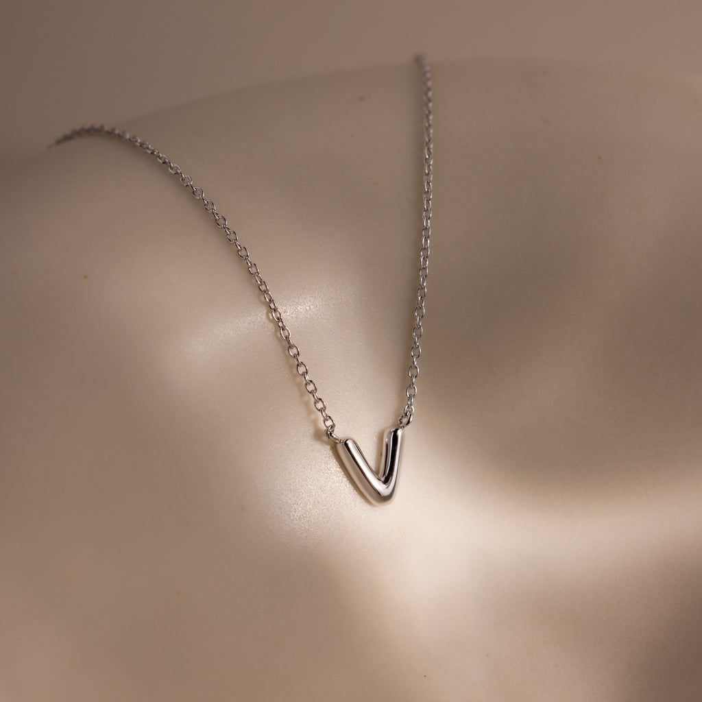 A Dainty Bubble Letter Necklace in Sterling Silver rests on smooth, light-colored skin under soft lighting.
