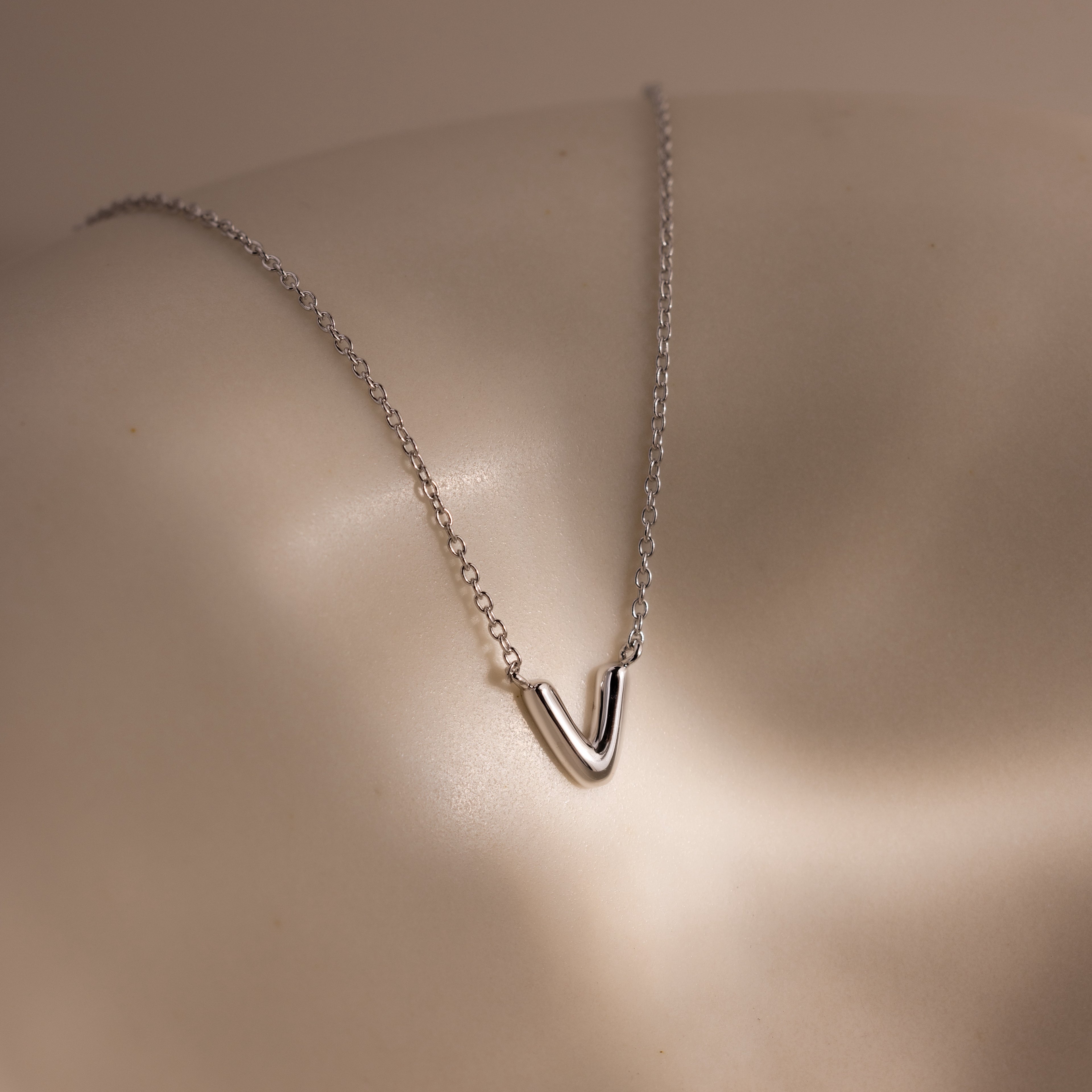 A Dainty Bubble Letter Necklace in Sterling Silver rests on smooth, light-colored skin under soft lighting.