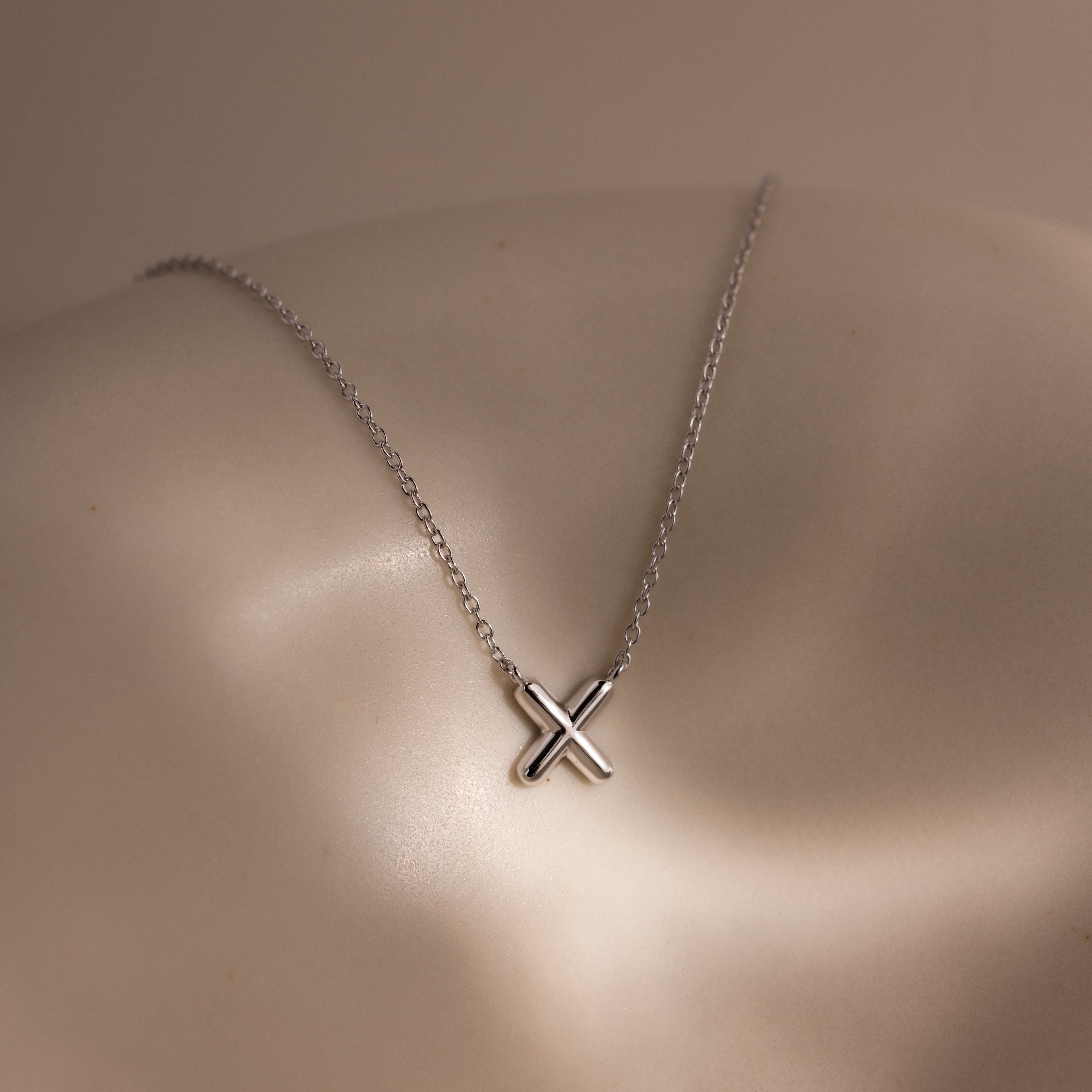 Dainty Bubble Letter Necklace in Sterling Silver, featuring a minimalist silver chain and small bubble letter pendant, displayed on a neutral, curved surface with soft lighting.