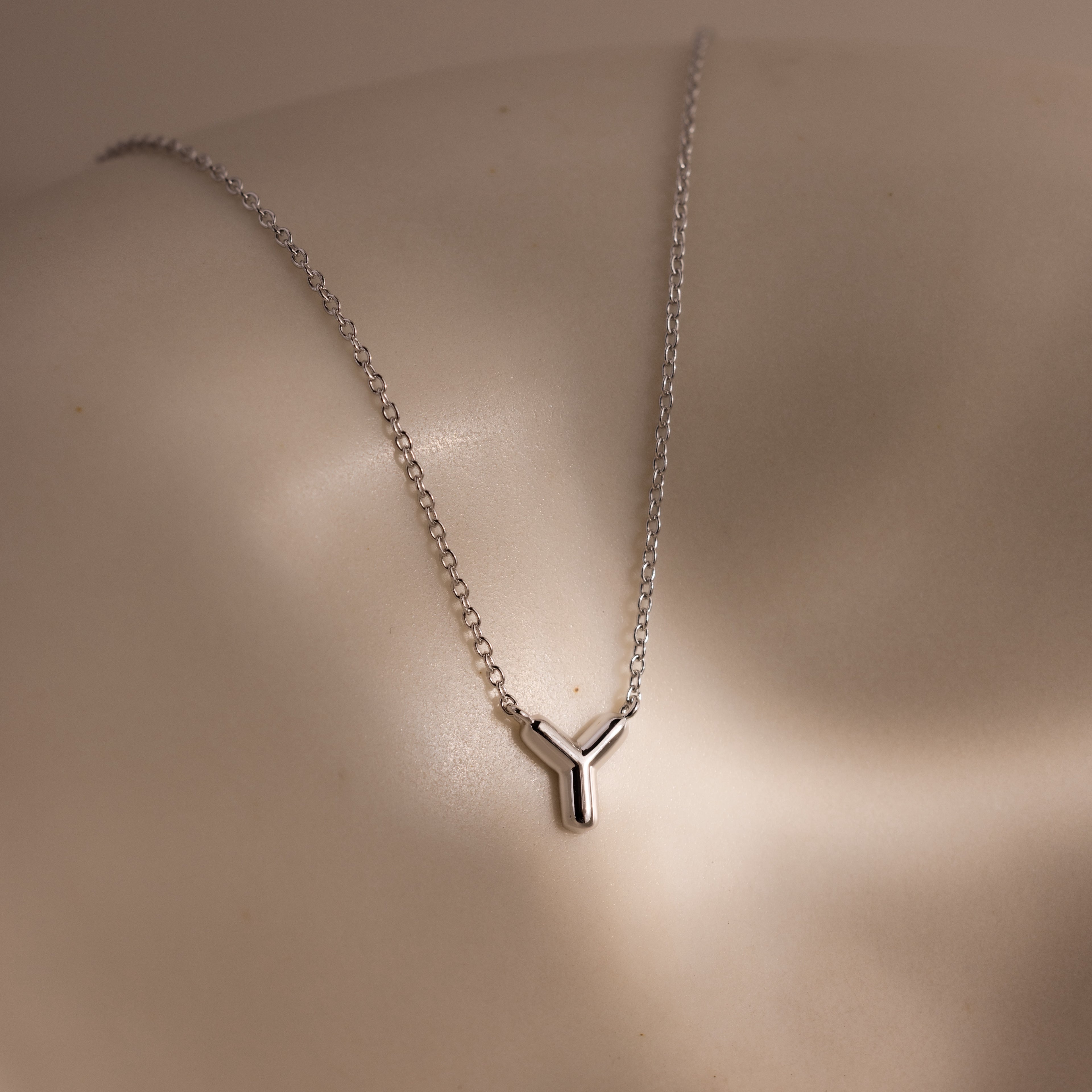The Dainty Bubble Letter Necklace in Sterling Silver is displayed on a smooth, light-colored surface with gentle, soft lighting.