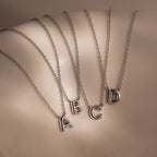 Four Dainty Bubble Letter Necklaces in Sterling Silver with letter pendants A, B, C, and D displayed on a curved surface—ideal as a personalized minimalist accessory for everyday style.