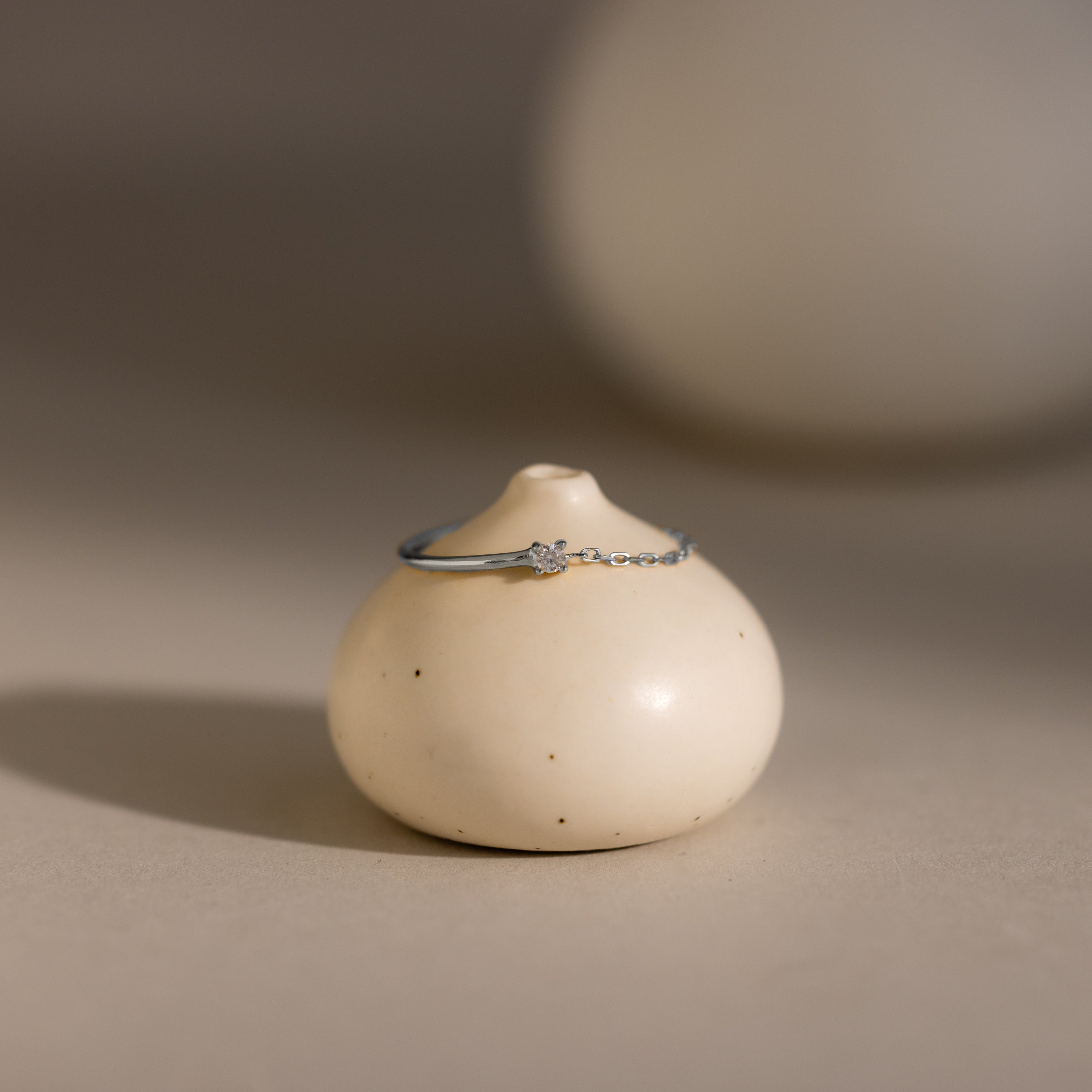 The Opal Half Chain Ring sits atop a small, round, beige ceramic object in gentle lighting—an ideal choice for fans of dainty jewelry.