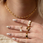 A hand with pearl and gold jewelry, nude nails with pearls, two layered gold necklaces with pearls, a boho jewelry vibe, and the elegant Cosmic Moonstone Ring as a statement piece.
