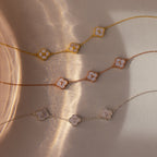 The Pearl Clover Letter Bracelet features delicate chain links, an initial letter charm, and a mother of pearl clover, all showcased on a neutral, sunlit background.