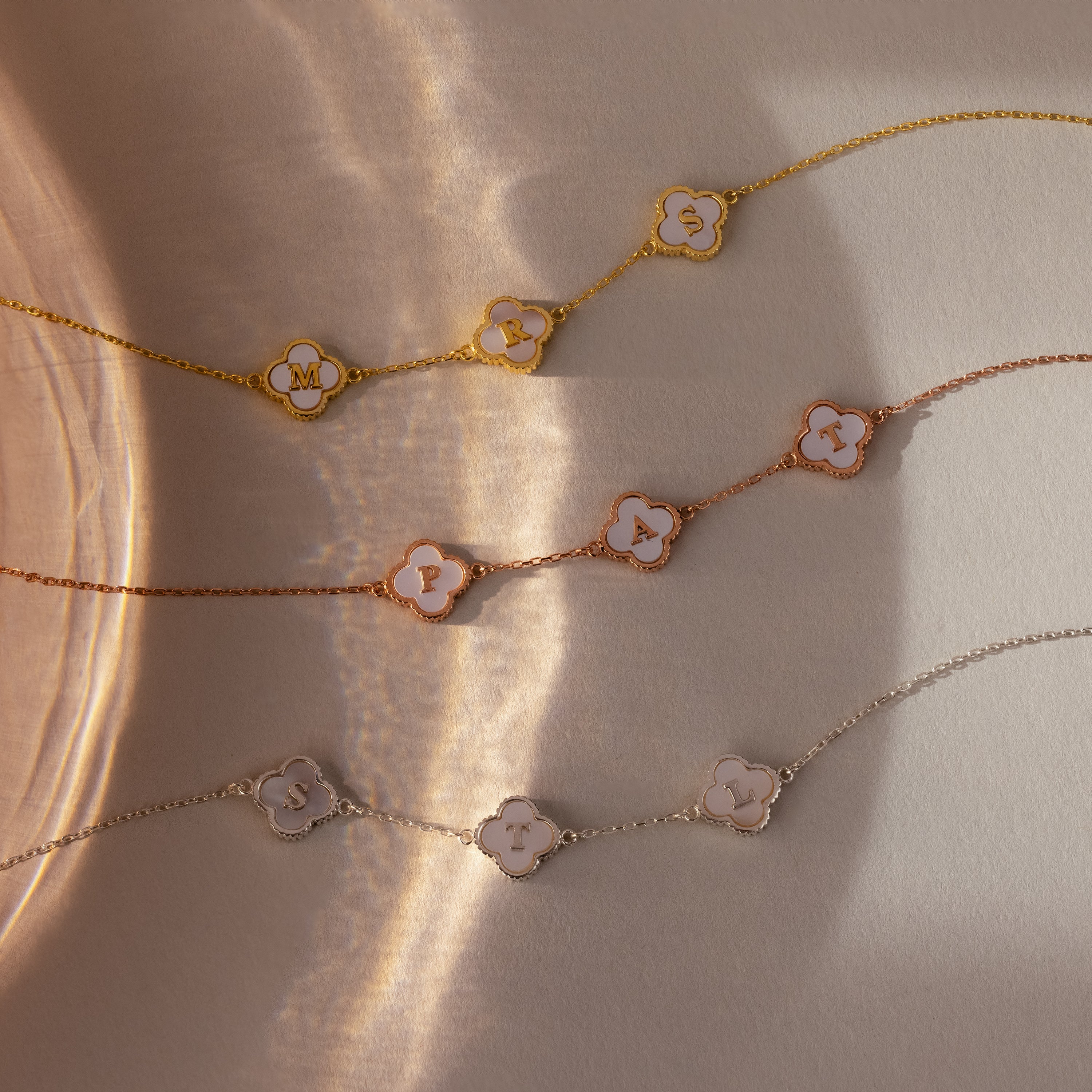 The Pearl Clover Letter Bracelet features delicate chain links, an initial letter charm, and a mother of pearl clover, all showcased on a neutral, sunlit background.