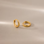Pair of 6mm tiny dainty gold huggie hoop earrings displayed on a neutral satin surface with soft lighting.