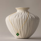 Gemstone Clover Necklace with green four-leaf clover pendant on delicate 18K gold chain displayed on textured white vase.