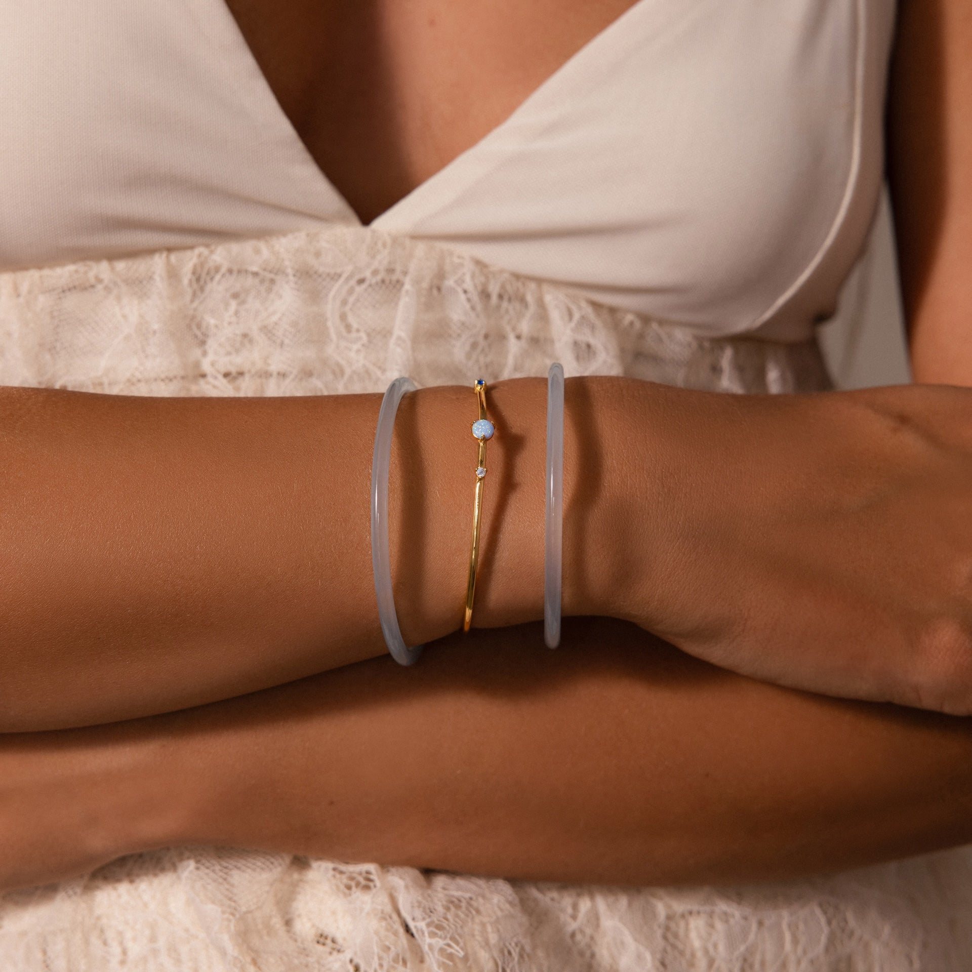 A woman in a white lace dress wears the Thin Blue Jade Bangle Set and a gold bracelet on her wrist.