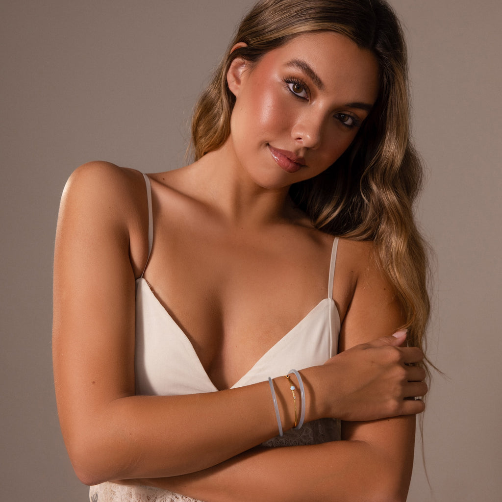 A woman in a white camisole poses confidently with her arms crossed, wearing the Thin Blue Jade Bangle Set and bracelets, looking directly at the camera.