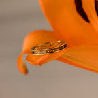 The Peridot Inlay Eternity Ring with rectangular stones is displayed on the petal of an orange lily flower.
