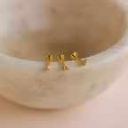 Three Tiny Diamond Flatback Studs with clear gemstones are arranged on the smooth edge of a beige marble bowl.