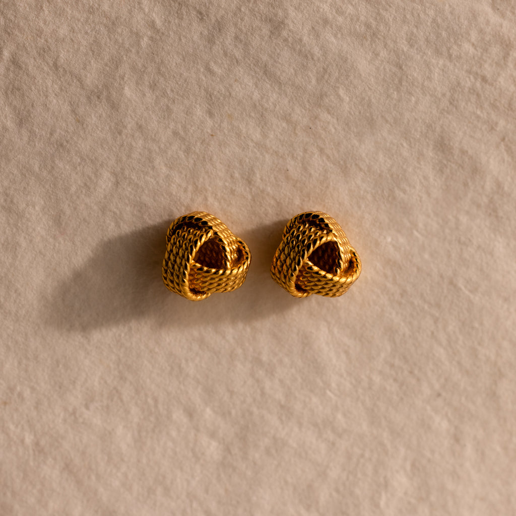 The Rope Knot Studs rest elegantly on a textured beige surface, showcasing timeless style and subtle sophistication.