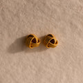 The Rope Knot Studs rest elegantly on a textured beige surface, showcasing timeless style and subtle sophistication.