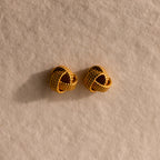The Rope Knot Studs rest elegantly on a textured beige surface, showcasing timeless style and subtle sophistication.