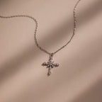 The Vintage Diamond Cross Necklace in Silver is displayed on a beige surface with soft shadow lines.