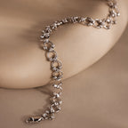 The Orbit Chain Bracelet, featuring textured circular links, is showcased on a smooth beige surface.