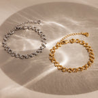 Two elegant Orbit Chain Bracelets—one silver, one gold—are displayed on a beige surface, enhanced by soft light reflections.