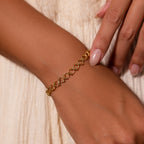 A hand adorned with the Orbit Chain Bracelet, featuring interlocking loops, rests on a cream-colored dress.