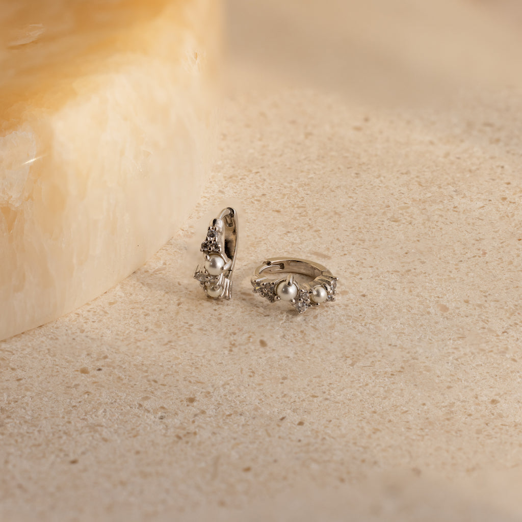 Pearl Diamond Cluster Huggies in Sterling Silver, reminiscent of elegant pearl and diamond earrings, displayed on a light, textured stone surface.