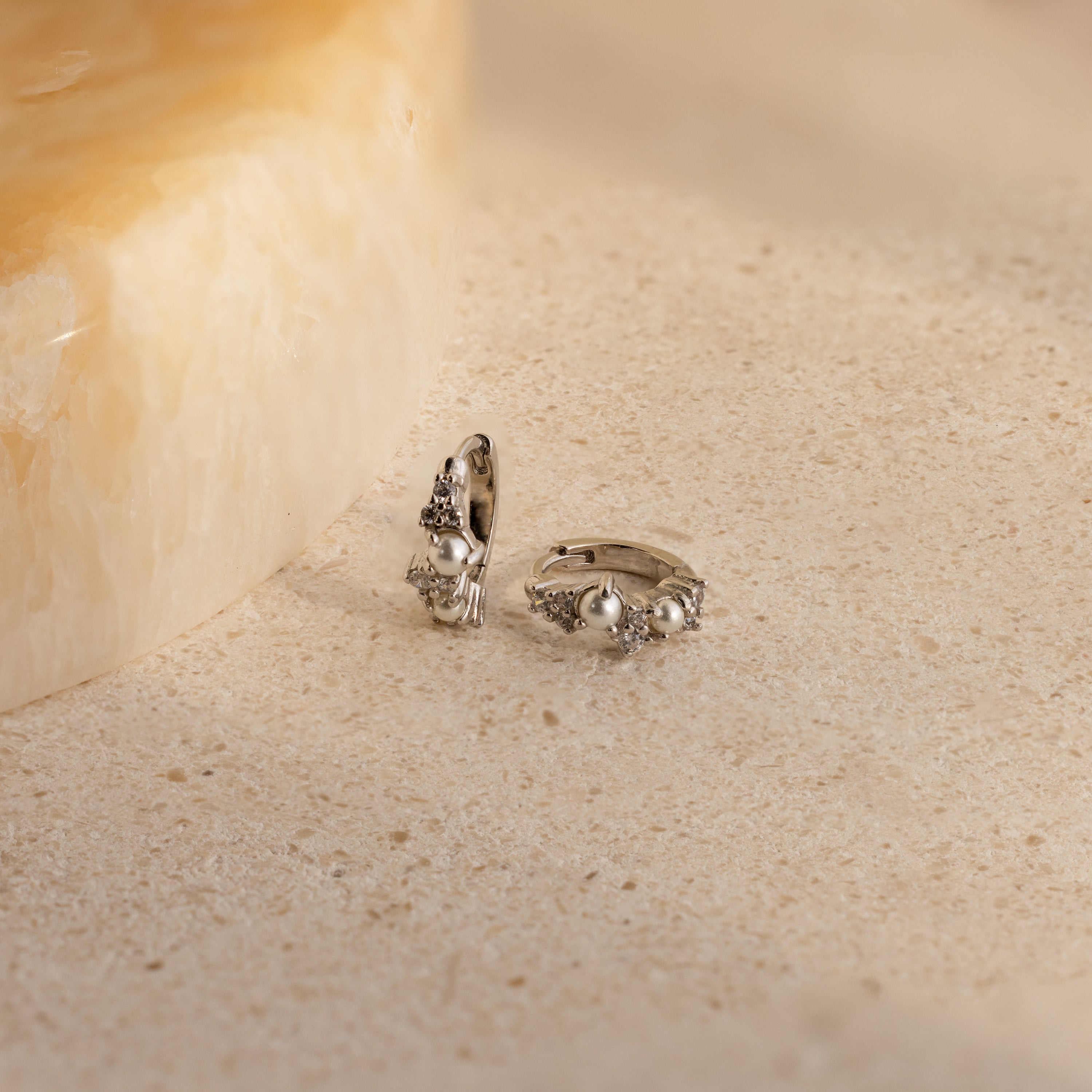 Pearl Diamond Cluster Huggies in Sterling Silver, reminiscent of elegant pearl and diamond earrings, displayed on a light, textured stone surface.