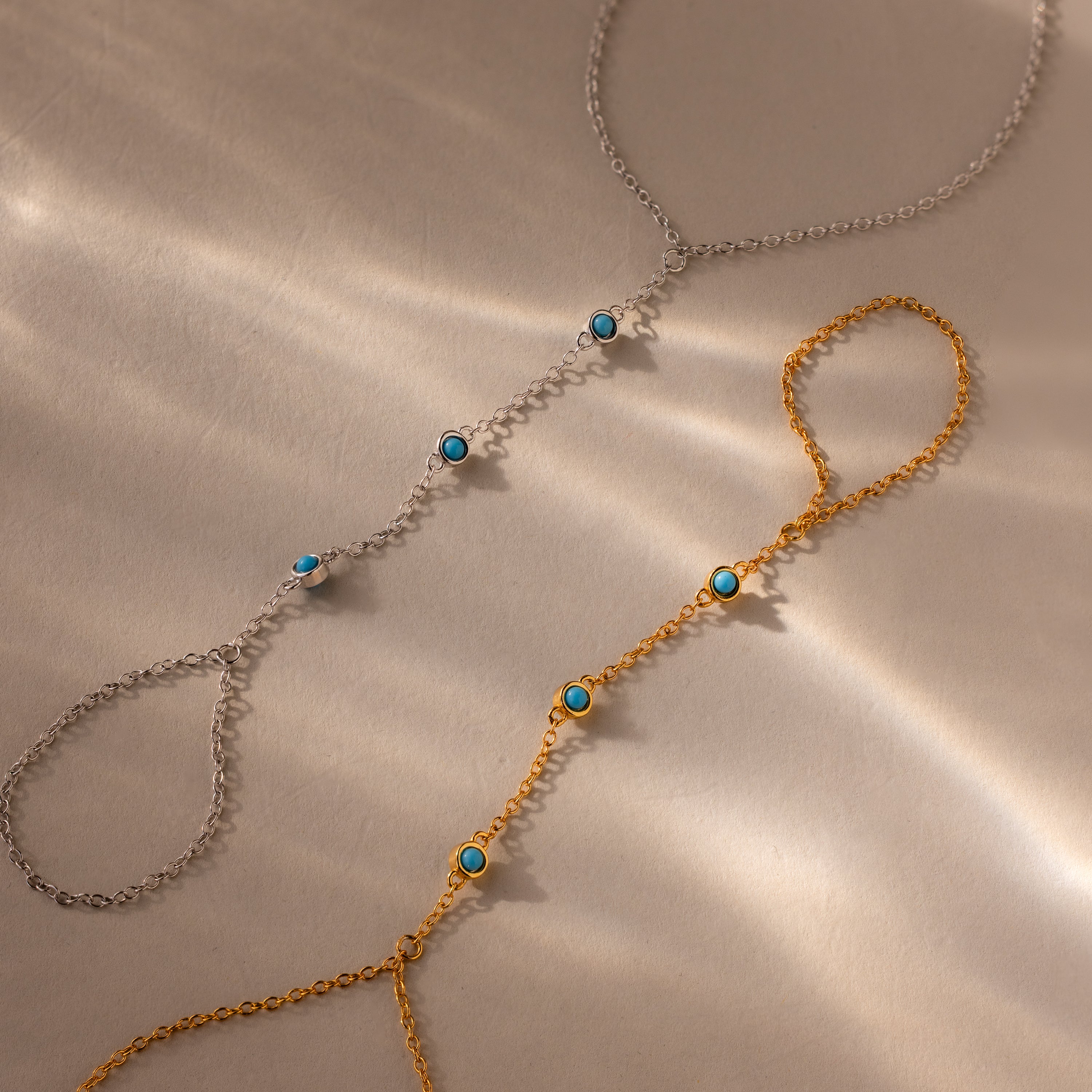 Two Turquoise Hand Chain Bracelets, one in silver and one in gold, each accented with turquoise stones, are displayed on a beige surface—the perfect set for fans of the Turquoise Hand Chain Bracelet.