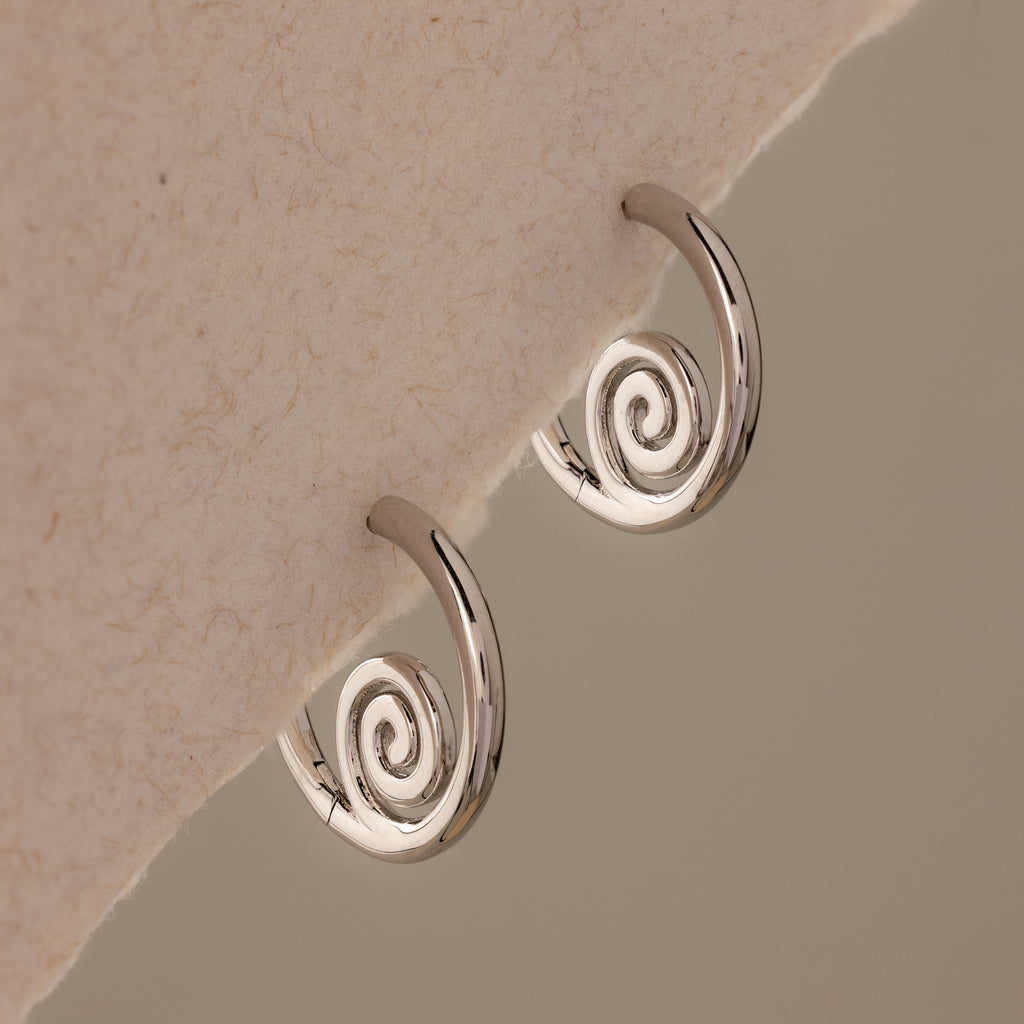 Spiral Swirl Hoops in Silver displayed on a textured off-white background—these beachy earrings are the perfect boho vacation jewelry accessory.