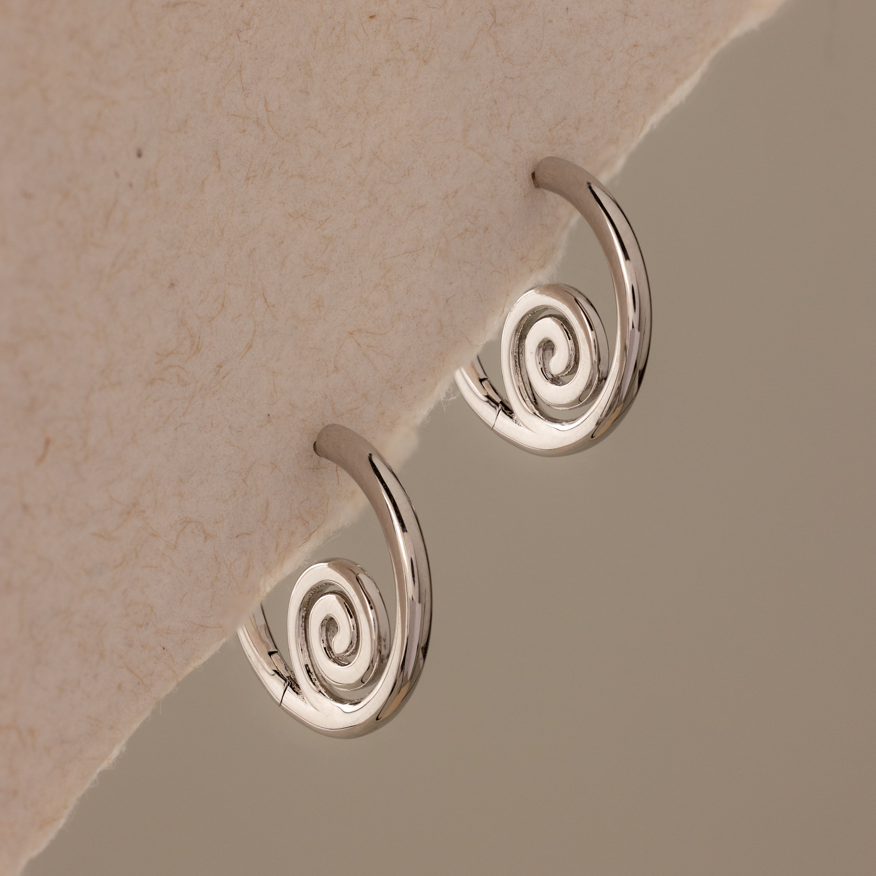 Spiral Swirl Hoops in Silver displayed on a textured off-white background—these beachy earrings are the perfect boho vacation jewelry accessory.
