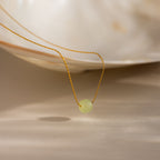 Close-up of a delicate gold chain necklace featuring a single round green jade bead, draped from a white shell dish.