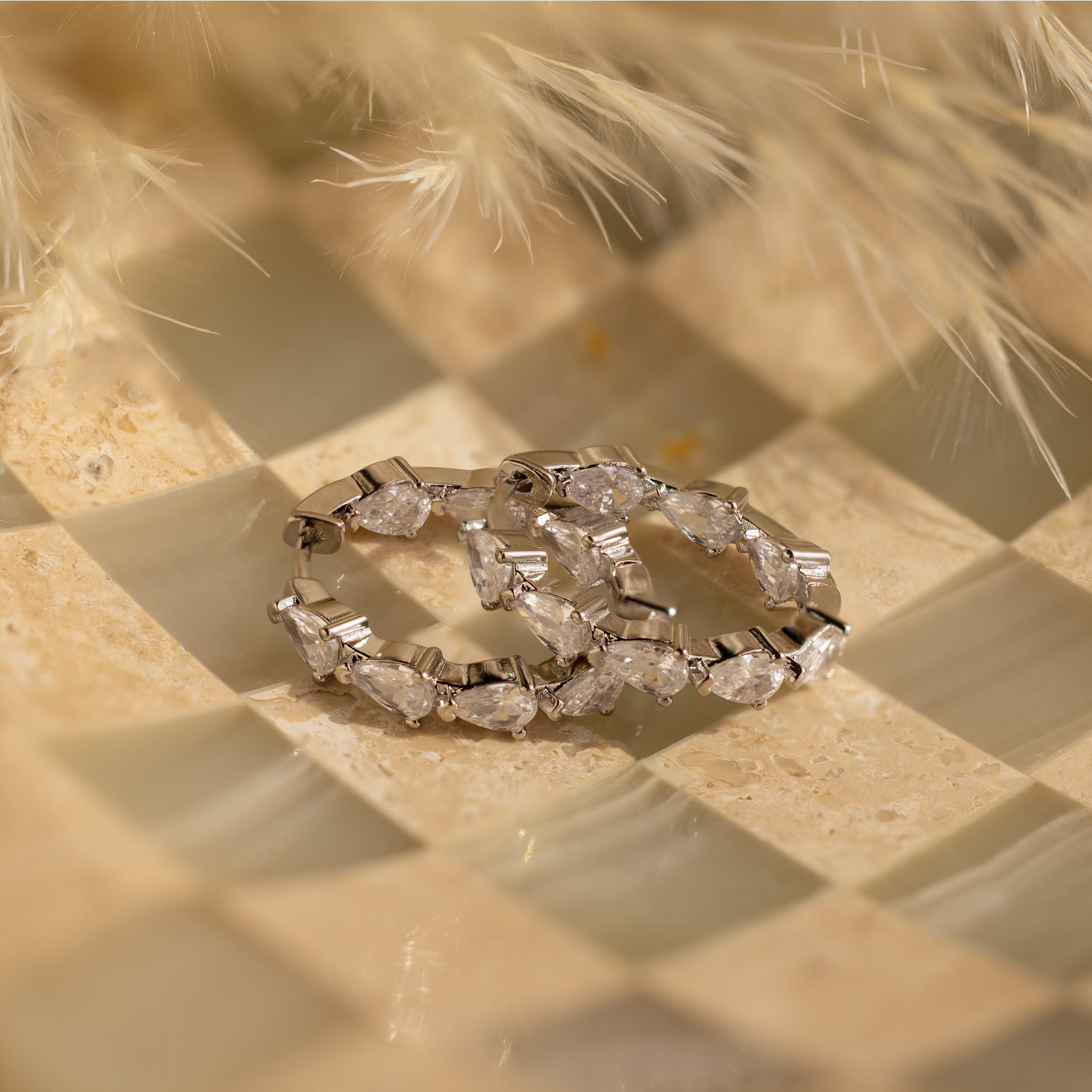Inside Out Pear Diamond Hoops, featuring teardrop-shaped CZ diamonds, are displayed on a checkered marble-style surface with soft beige accents.
